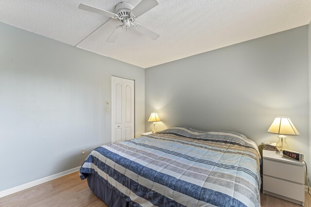 bedroom with a textured ceiling, wood finished floors, baseboards, and a ceiling fan