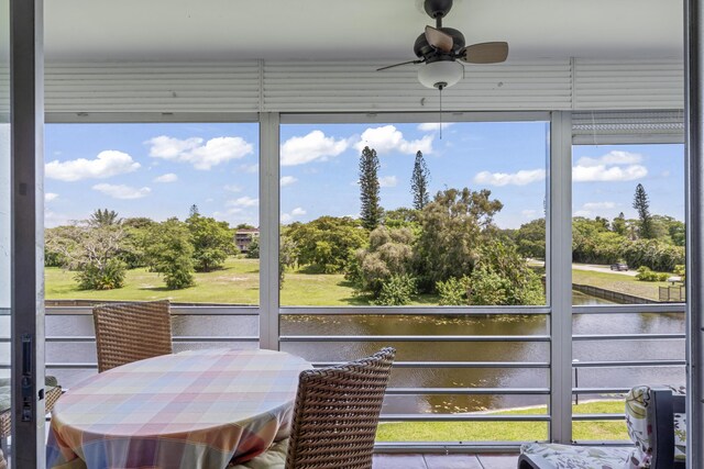 sunroom / solarium with a water view, ceiling fan, and view of scattered trees