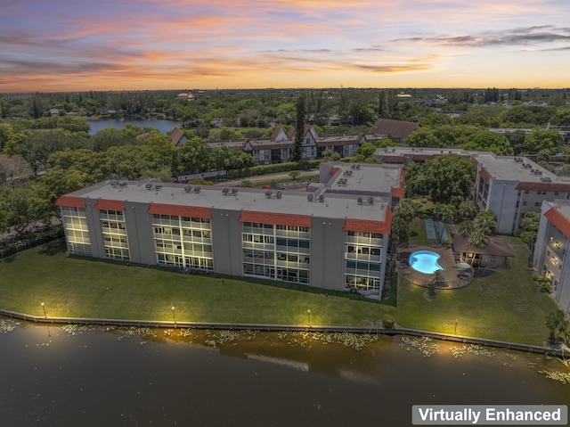 aerial view at dusk of a water view, view of pool area, and view of wooded area
