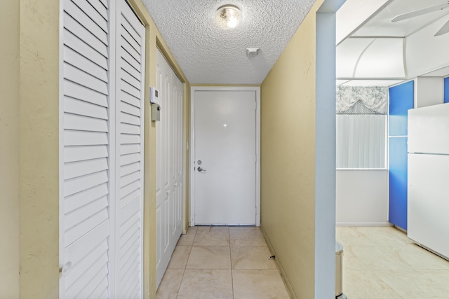 hallway with a textured ceiling, tile patterned floors, and baseboards