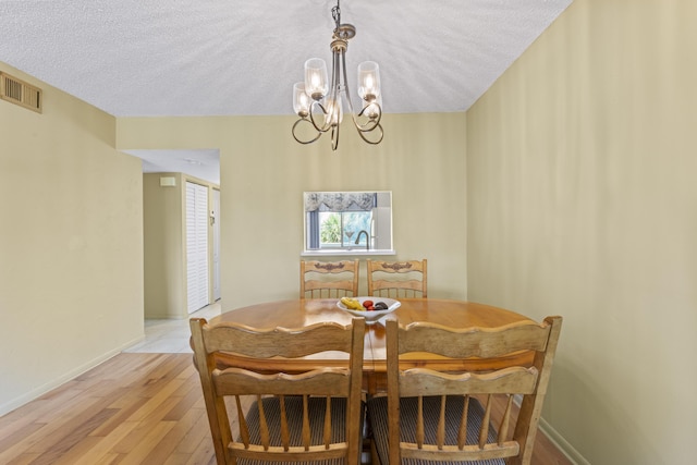 dining space featuring a chandelier, light wood-style floors, a textured ceiling, and baseboards