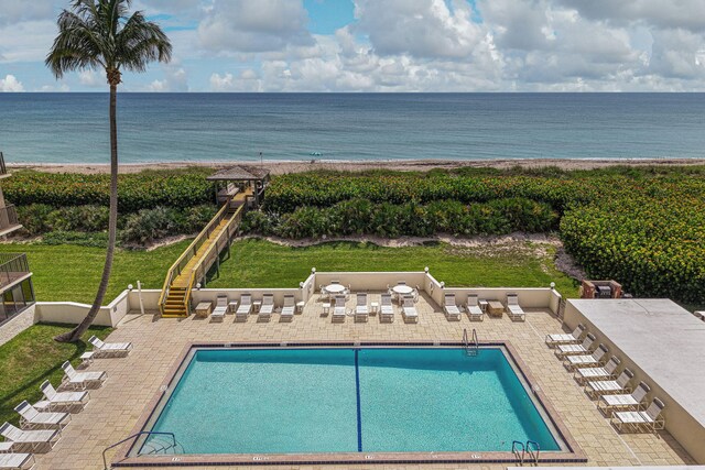 community pool featuring view of water and beach, a patio area, and stairs