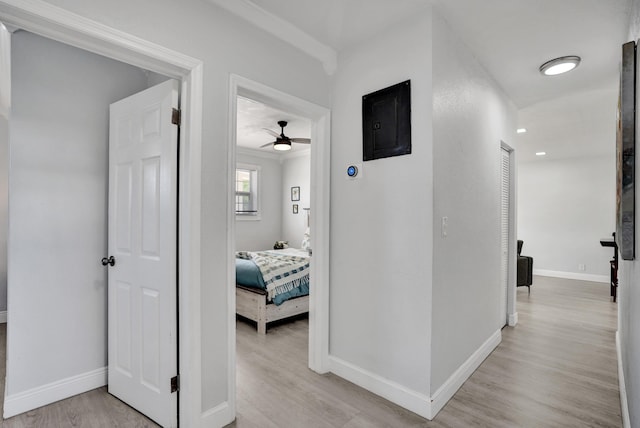 corridor featuring electric panel, light wood-type flooring, and baseboards
