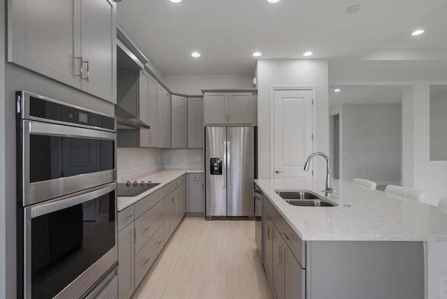 kitchen featuring appliances with stainless steel finishes, gray cabinetry, a sink, an island with sink, and recessed lighting