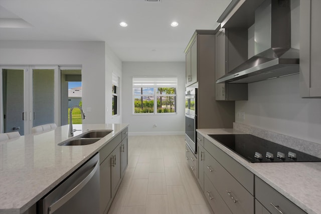 kitchen featuring wall chimney range hood, a sink, stainless steel appliances, baseboards, and gray cabinetry