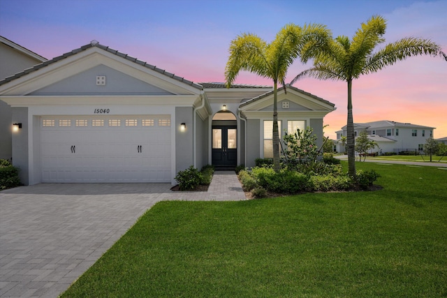 view of front facade with french doors, decorative driveway, a yard, a tiled roof, and an attached garage