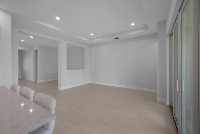 interior space with a raised ceiling, recessed lighting, baseboards, and light wood-style floors