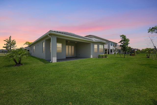 rear view of house featuring a lawn, stucco siding, a patio, metal roof, and a standing seam roof