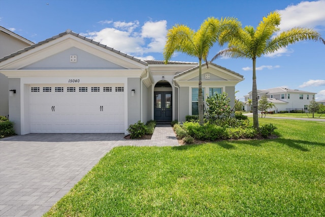 view of front of property featuring french doors, decorative driveway, a front lawn, stucco siding, and a tiled roof