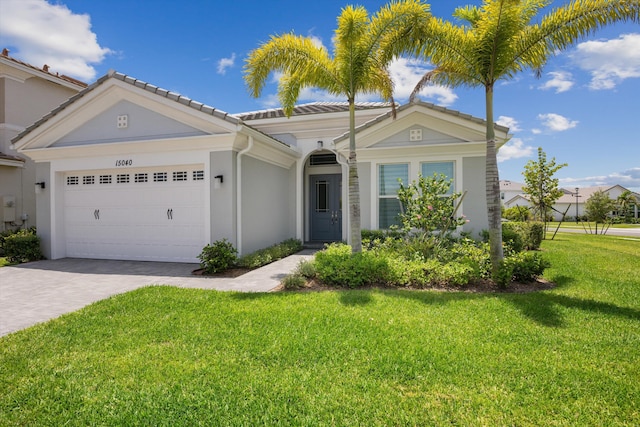 single story home featuring decorative driveway, an attached garage, a front yard, a tiled roof, and stucco siding