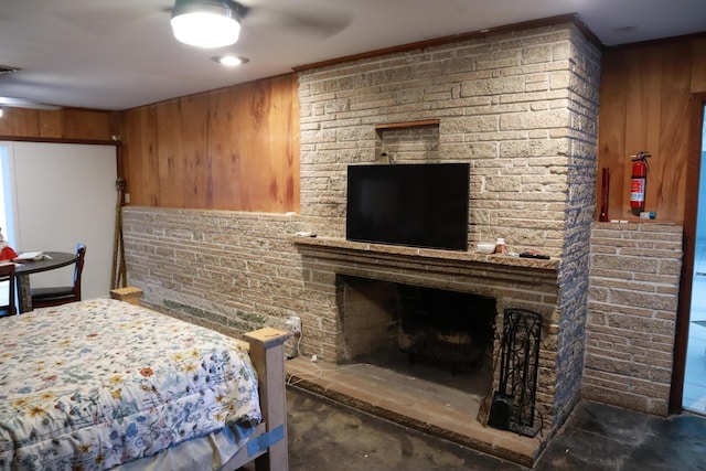 bedroom with a fireplace, concrete floors, wooden walls, and a ceiling fan