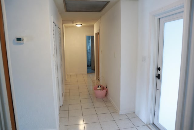 hallway featuring light tile patterned floors, baseboards, and attic access