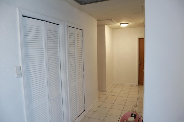 hall featuring light tile patterned floors, attic access, and baseboards