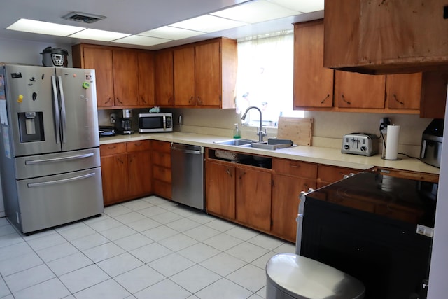 kitchen featuring appliances with stainless steel finishes, a sink, brown cabinetry, and light countertops