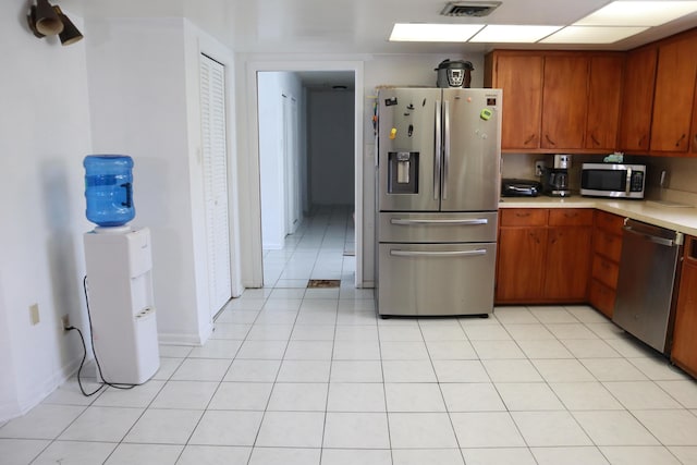 kitchen with stainless steel appliances, light countertops, brown cabinets, baseboards, and light tile patterned flooring