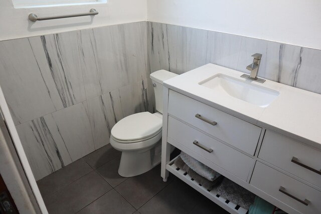 bathroom featuring vanity, toilet, tile patterned flooring, tile walls, and a wainscoted wall