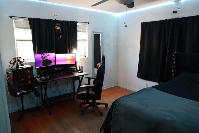 bedroom with wood finished floors, multiple windows, an office area, and baseboards