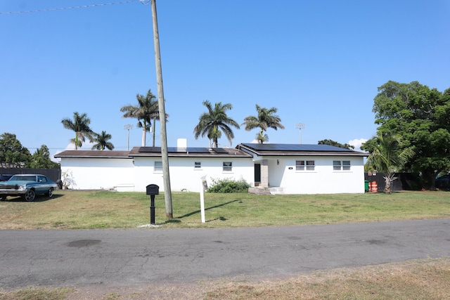 ranch-style home featuring roof mounted solar panels, a front yard, and stucco siding