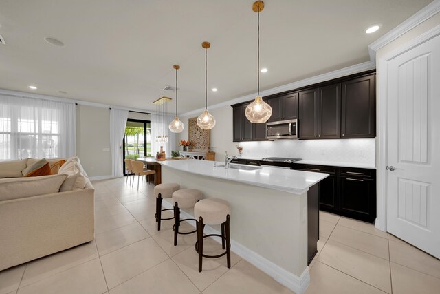kitchen with stainless steel microwave, open floor plan, a sink, a kitchen bar, and light countertops