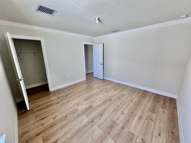 unfurnished bedroom featuring a textured ceiling, light wood-style flooring, crown molding, baseboards, and a closet