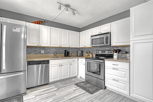 kitchen with stainless steel appliances, a sink, light countertops, white cabinets, and tasteful backsplash