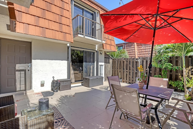 view of patio with a balcony, fence, and outdoor dining space