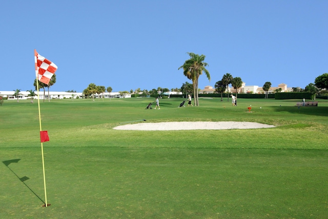 view of property's community with golf course view, a putting area, and a lawn