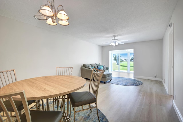 dining space with light wood-type flooring, a ceiling fan, a textured ceiling, a chandelier, and baseboards