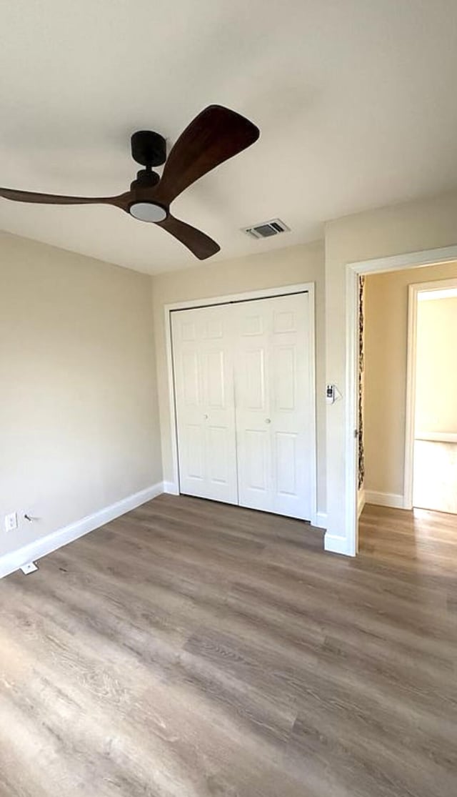 unfurnished bedroom featuring baseboards, wood finished floors, a closet, and a ceiling fan