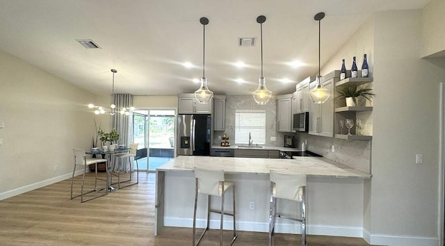 kitchen with stainless steel appliances, a sink, a peninsula, open shelves, and light wood-type flooring