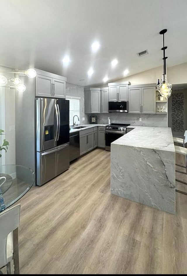 kitchen featuring stainless steel appliances, a sink, gray cabinetry, a peninsula, and light wood-style flooring