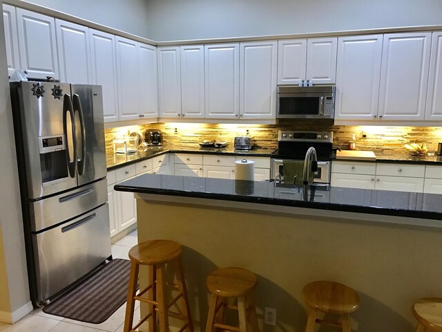 1366 Crossbill Ct, Weston, FL 33327 - kitchen with appliances with stainless steel finishes, backsplash, a kitchen bar, light tile patterned floors, and dark stone countertops