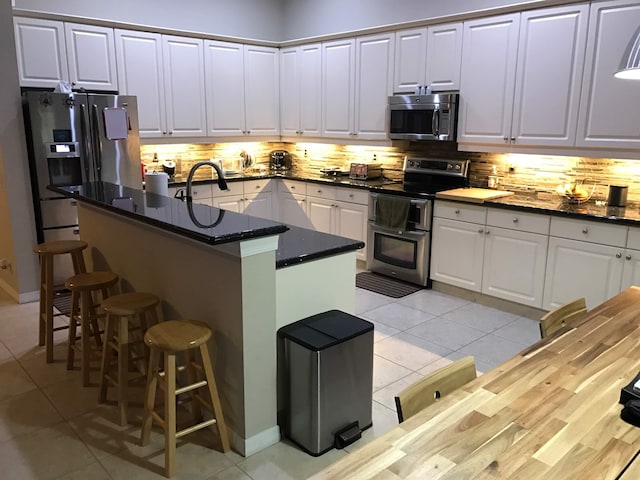 1366 Crossbill Ct, Weston, FL 33327 - kitchen with stainless steel appliances, light tile patterned flooring, a breakfast bar area, and tasteful backsplash