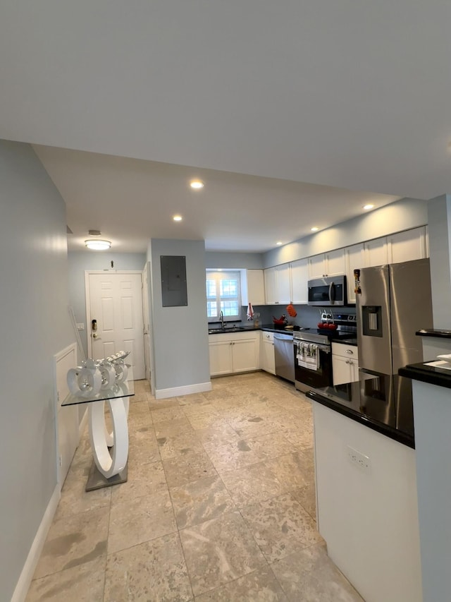 kitchen featuring appliances with stainless steel finishes, electric panel, white cabinets, dark countertops, and baseboards