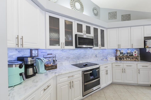 kitchen featuring stainless steel microwave, black electric cooktop, tasteful backsplash, white cabinets, and lofted ceiling