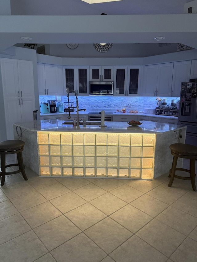 kitchen featuring light tile patterned floors, fridge with ice dispenser, stainless steel microwave, and glass insert cabinets