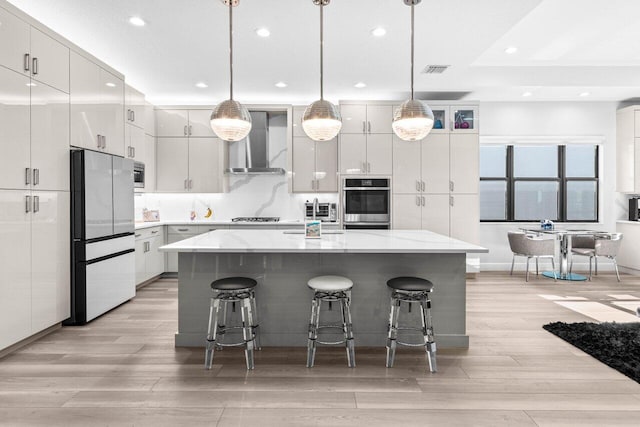 9333 Mountain Pine Grv, Boynton Beach, FL 33473 - kitchen featuring appliances with stainless steel finishes, wall chimney exhaust hood, light wood finished floors, a kitchen breakfast bar, and a center island