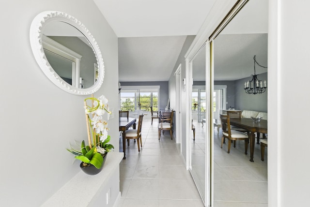 hall featuring light tile patterned floors, a chandelier, and baseboards