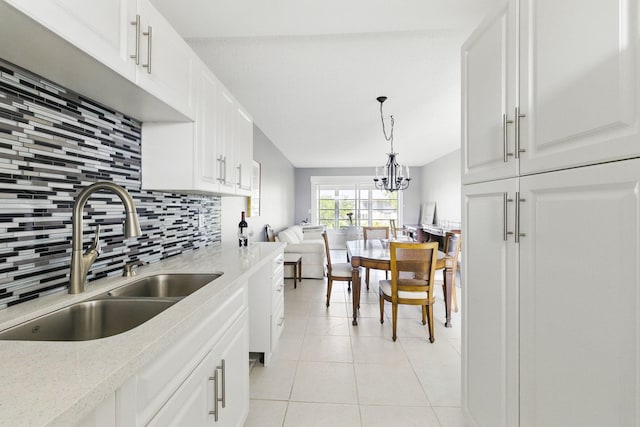 kitchen featuring a sink, backsplash, light tile patterned floors, white cabinets, and a chandelier