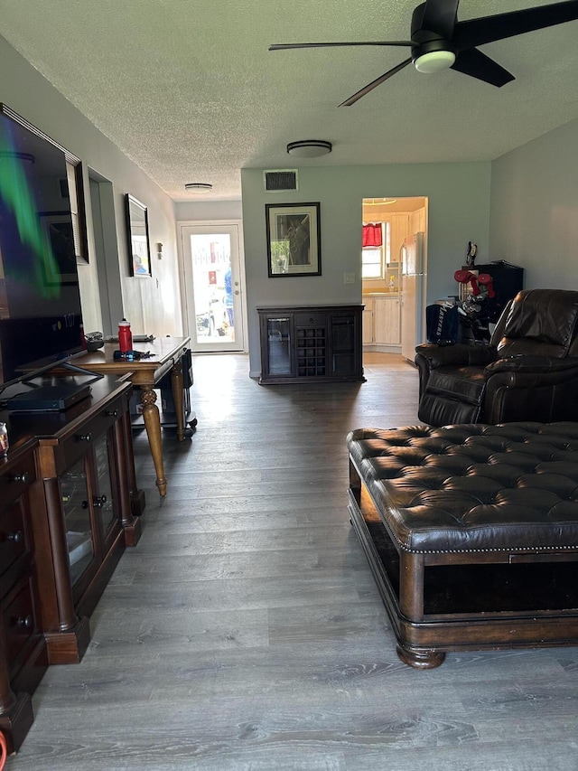 living room with ceiling fan, wood finished floors, and a textured ceiling