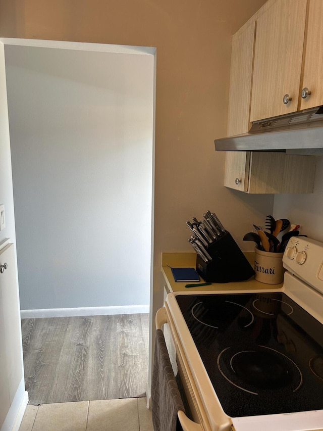 kitchen with white electric range oven, under cabinet range hood, light brown cabinetry, light wood-type flooring, and baseboards