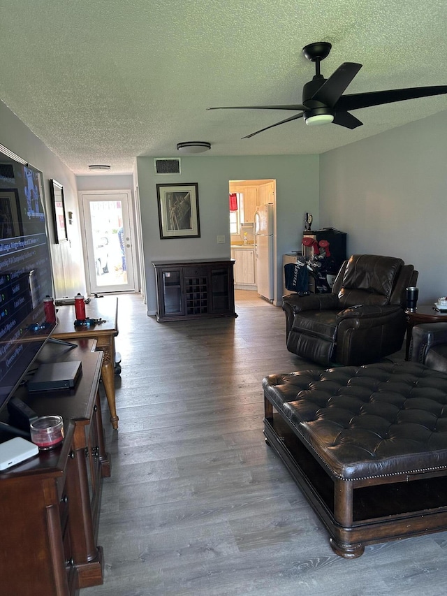 living area featuring a textured ceiling, ceiling fan, wood finished floors, and plenty of natural light