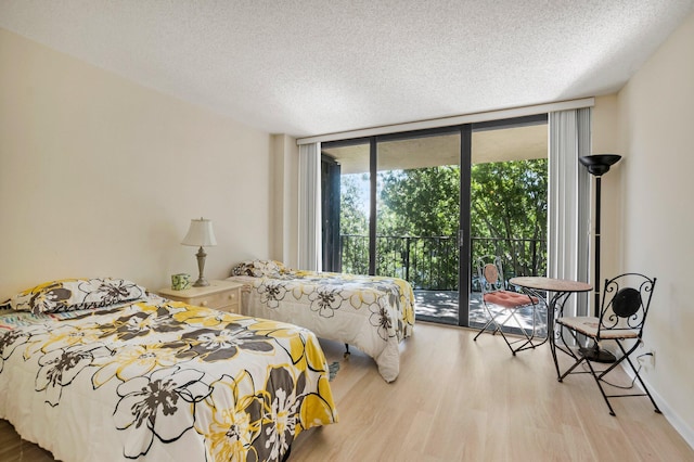 bedroom featuring a wall of windows, access to outside, wood finished floors, and a textured ceiling