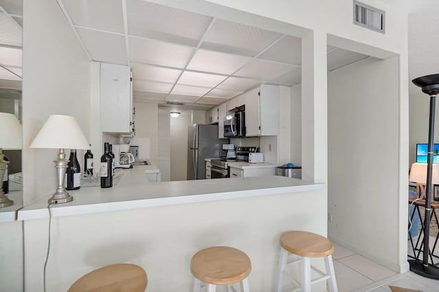 kitchen featuring stainless steel appliances, a drop ceiling, light countertops, a peninsula, and white cabinetry