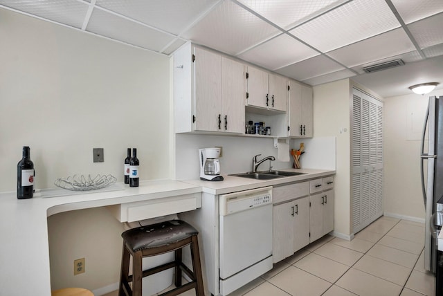 kitchen with white dishwasher, a sink, light countertops, light tile patterned floors, and baseboards