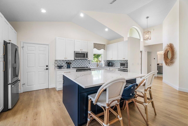 12811 Oak Knoll Dr, Palm Beach Gardens, FL 33418 - kitchen featuring appliances with stainless steel finishes, a breakfast bar, light stone counters, white cabinets, and light wood-type flooring