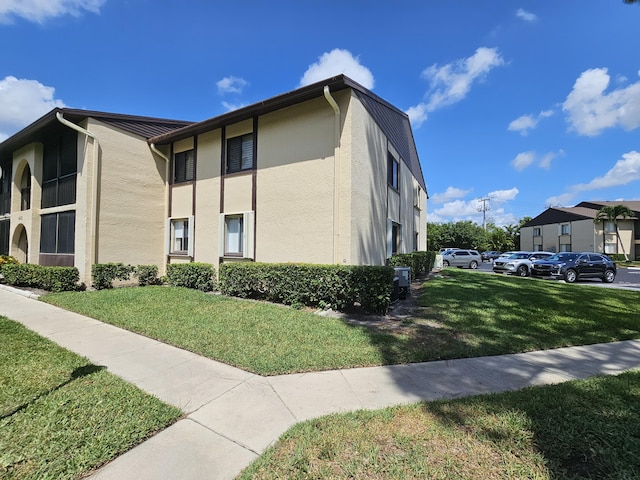 view of side of home featuring stucco siding, a lawn, and uncovered parking