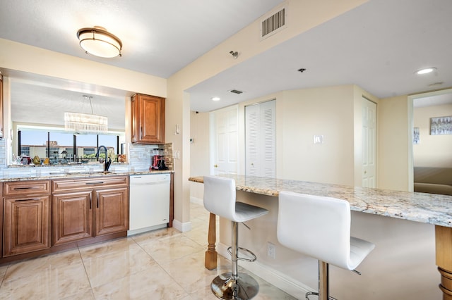 7290 Kinghurst Dr Unit 607, Delray Beach, FL 33446 - kitchen with white dishwasher, light stone counters, brown cabinets, a kitchen bar, and decorative backsplash