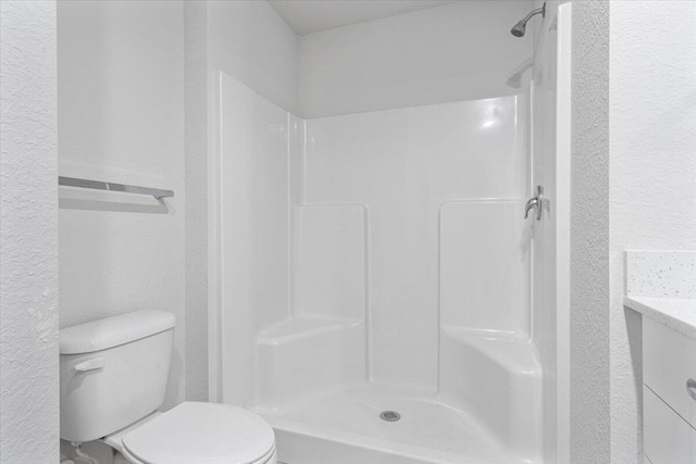 full bathroom featuring a textured wall, toilet, a shower, and vanity