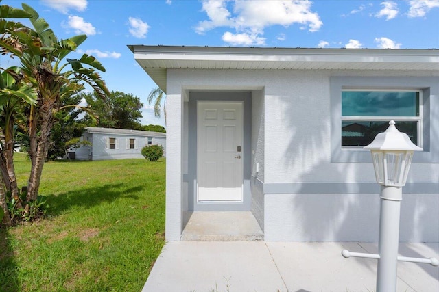 view of exterior entry featuring a yard and stucco siding